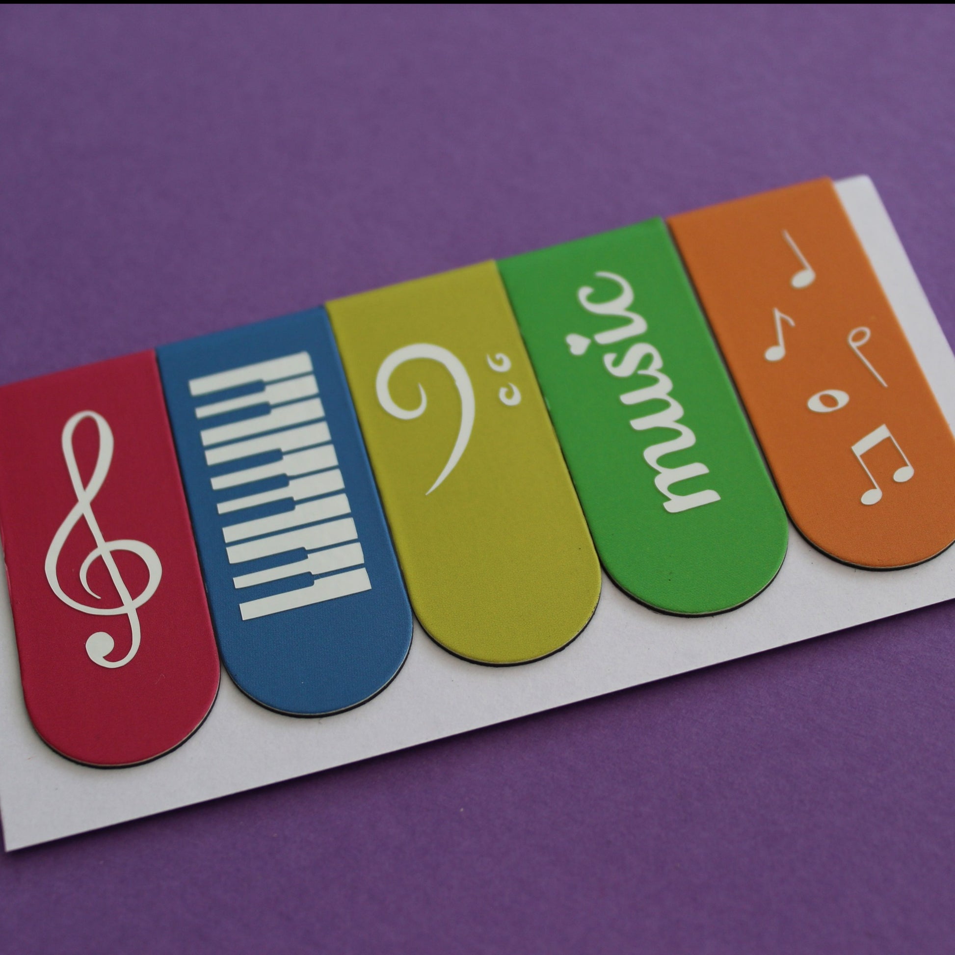 Bookmarks in pink, blue, yellow, green and orange. Each bookmark has a different symbol; treble clef, piano keys, bass clef, 'music' and music notes.