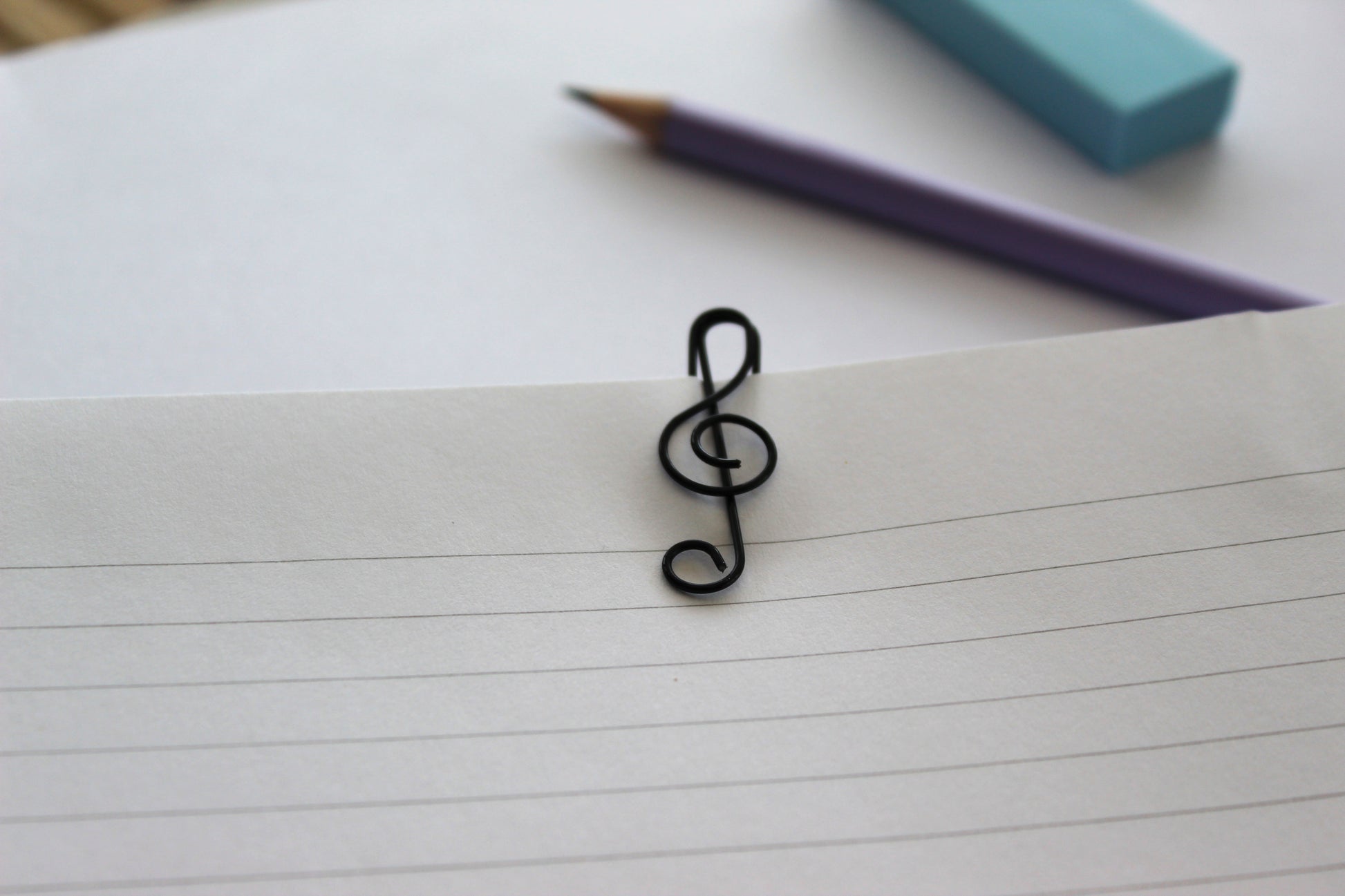 A black treble clef paperclip on a sheet of lined paper.