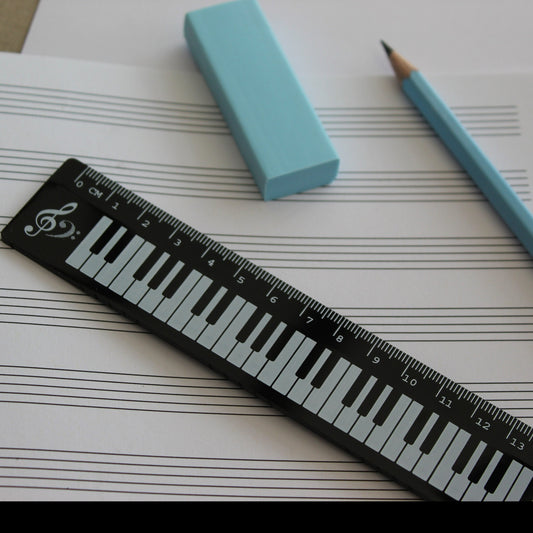 Black ruler with a piano keyboard. Manuscript paper, a pencil and a rubber in the background.