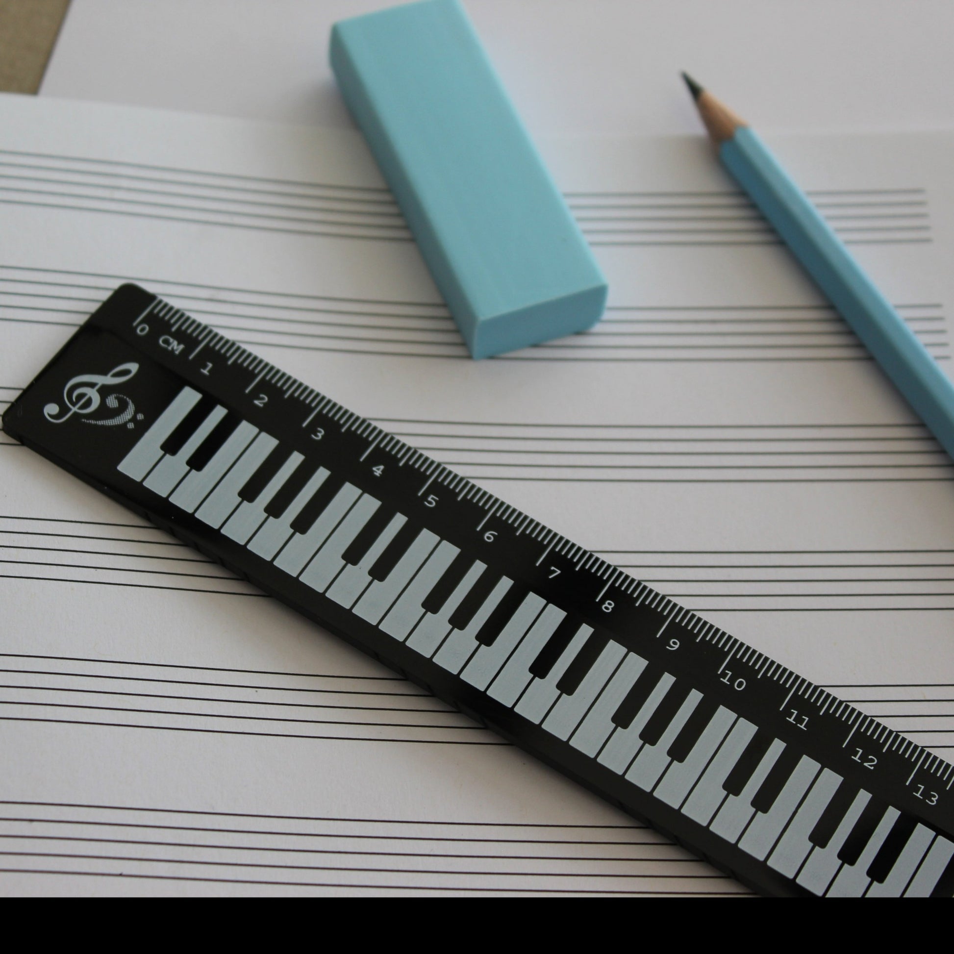 Black ruler with a piano keyboard. Manuscript paper, a pencil and a rubber in the background.