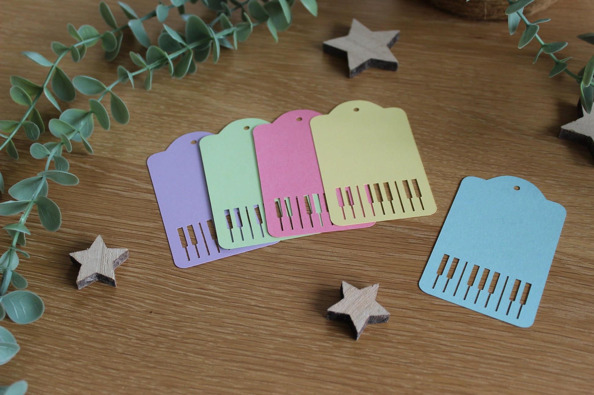 Pastel gift tags (purple, green, pink, yellow and blue) with piano keys cut out. Displayed on a wooden background with foliage and stars.