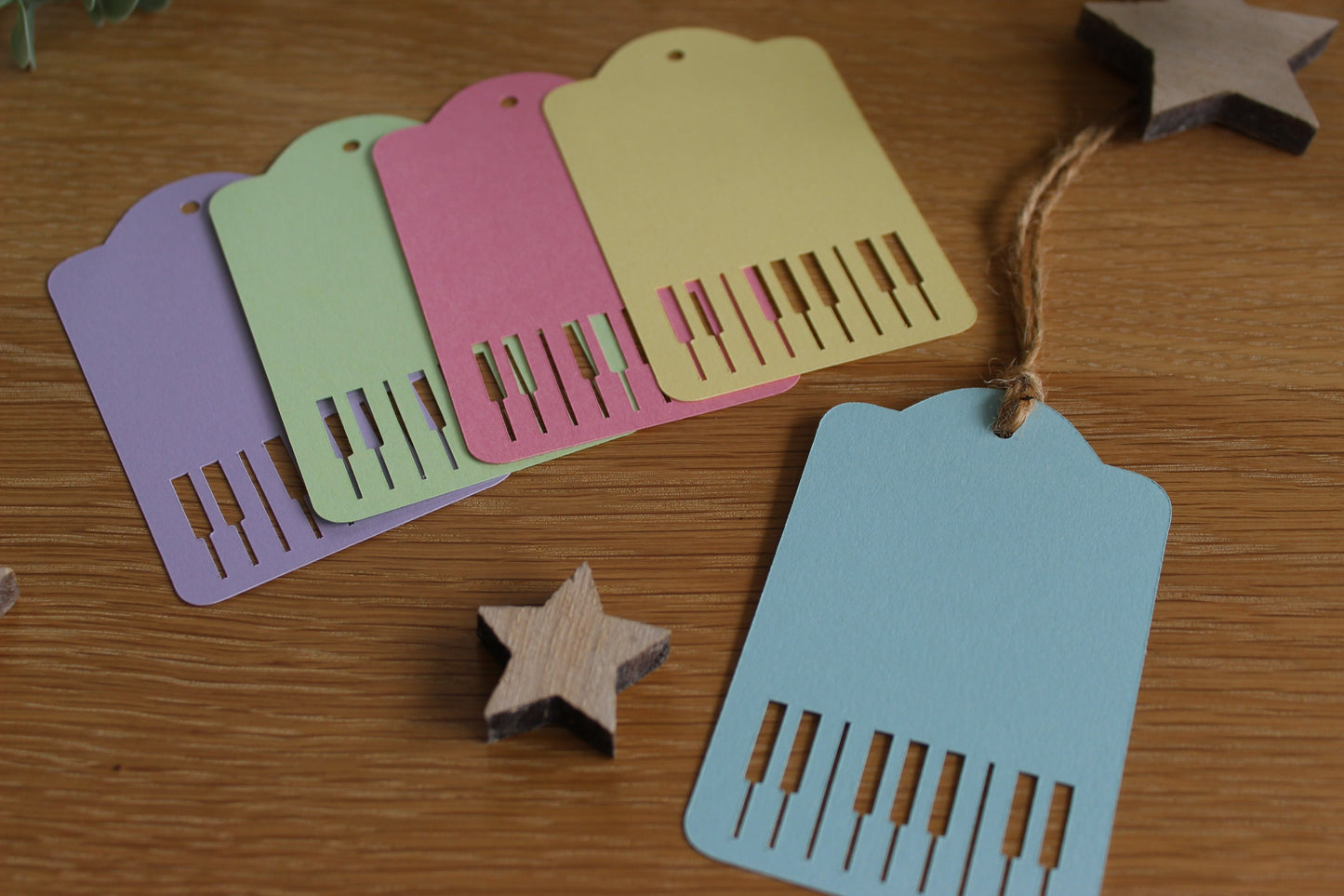 Pastel gift tags (purple, green, pink, yellow and blue) with piano keys cut out. Displayed on a wooden background with stars.