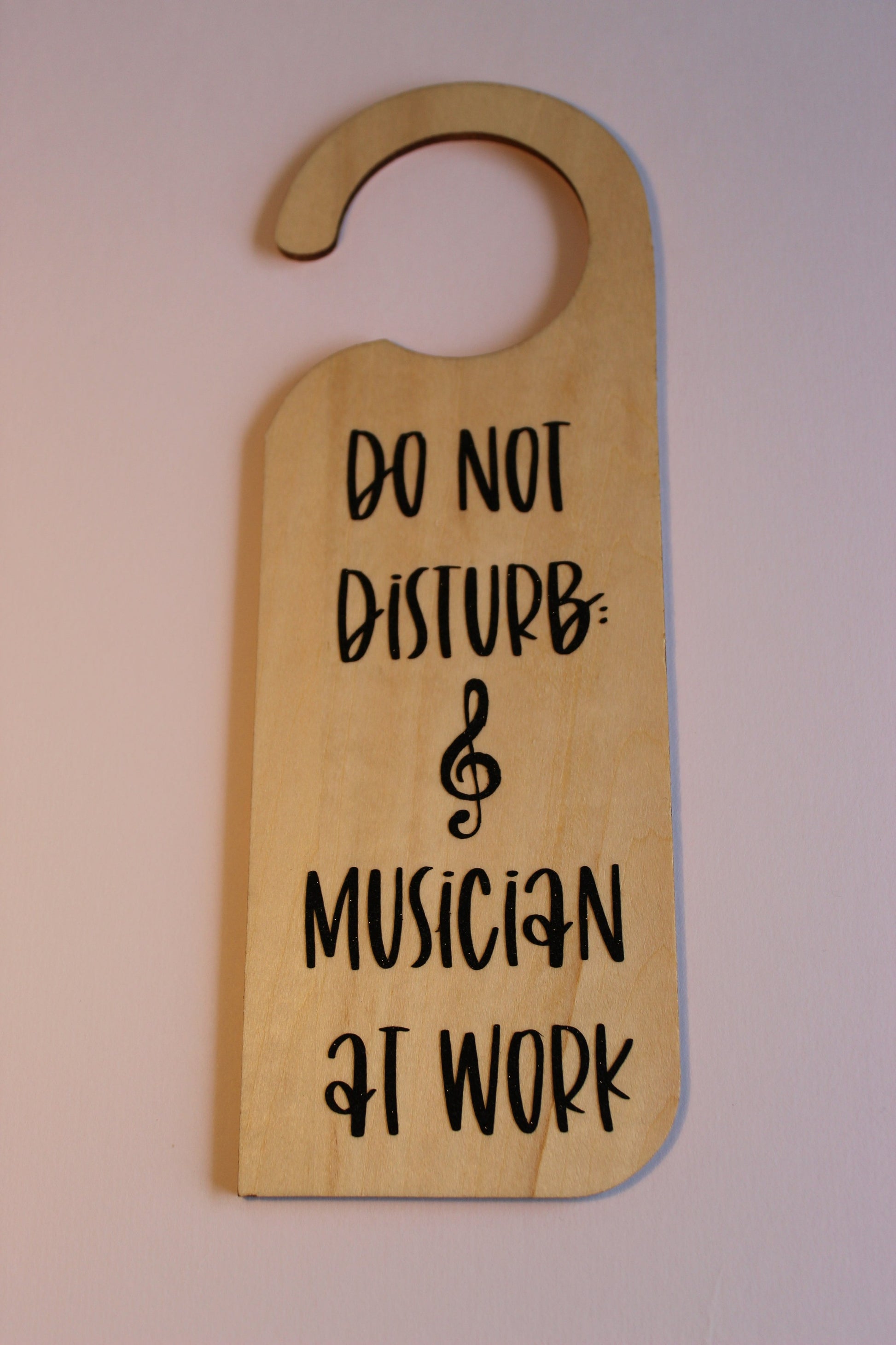 A wooden door hanger, displaying the text 'Do not disturb: musician at work' in black shimmer vinyl