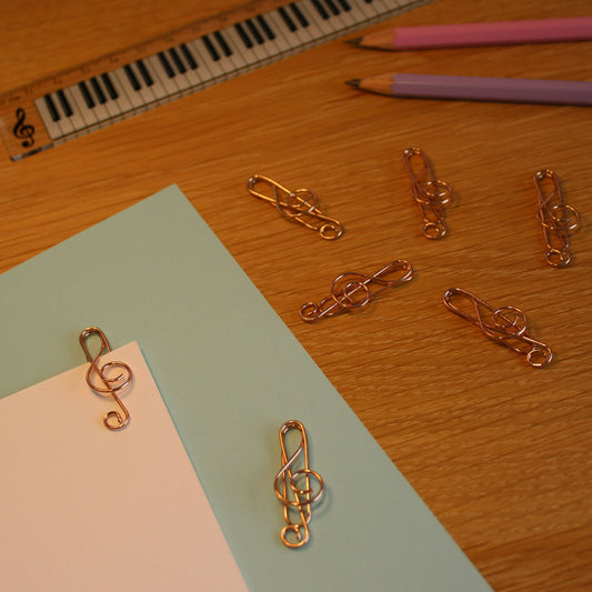 Several rose gold paperclips scattered on a desk. One attached to a piece of card. Pencils and a ruler in the background.
