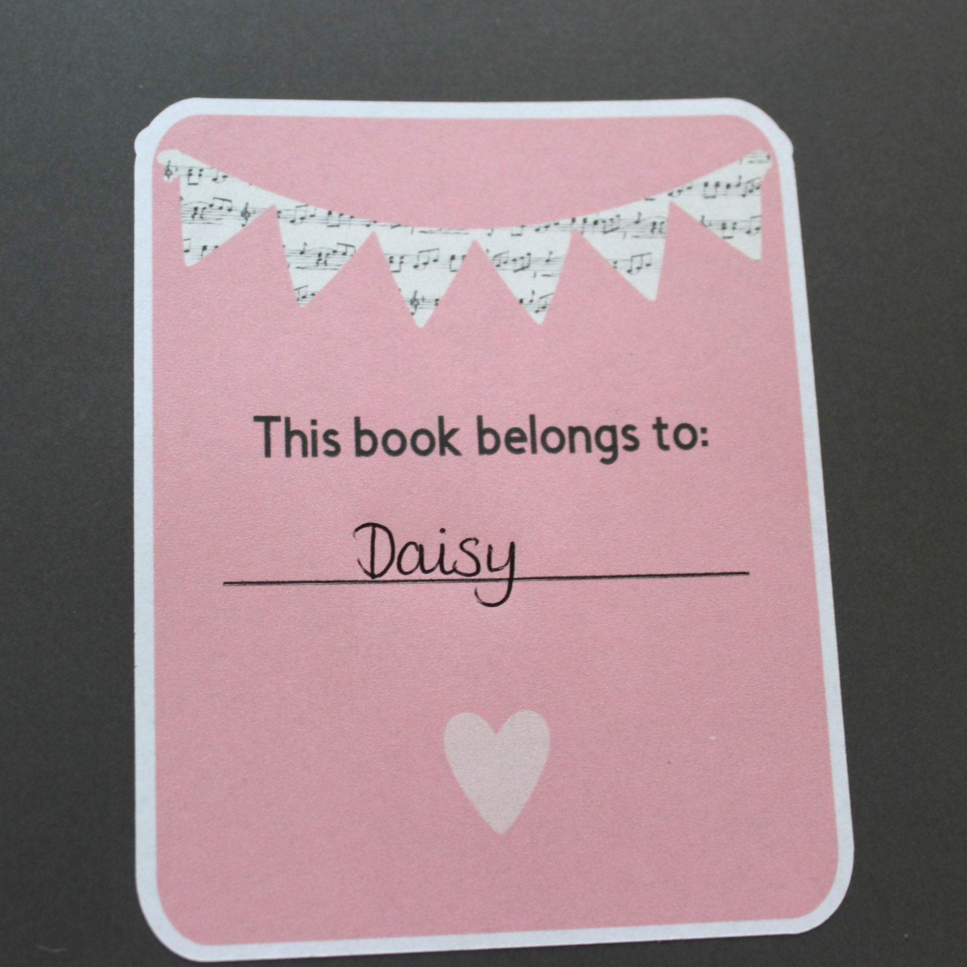 A pink bookplate with music bunting at the top and a heart below the text.