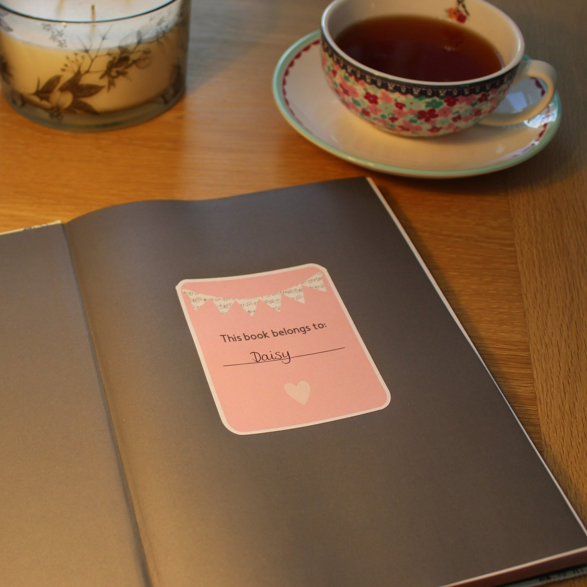 Pink bookplate with music bunting displayed in the front of a book. A cup of tea in the background