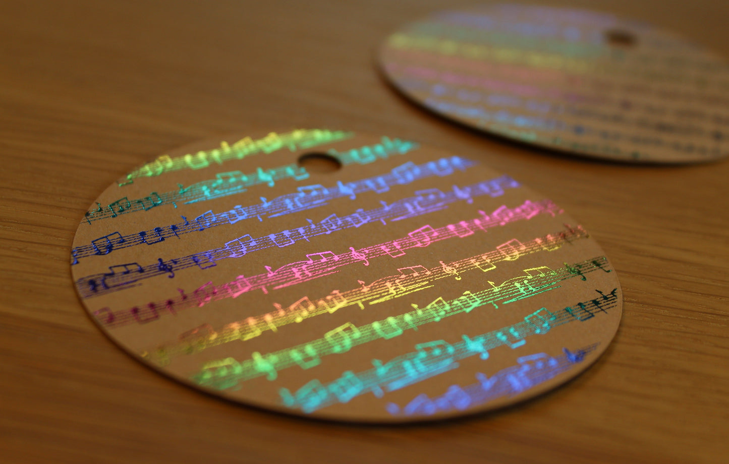 Round brown kraft gift tag. Design of rows of music in a multicoloured shiny foil.