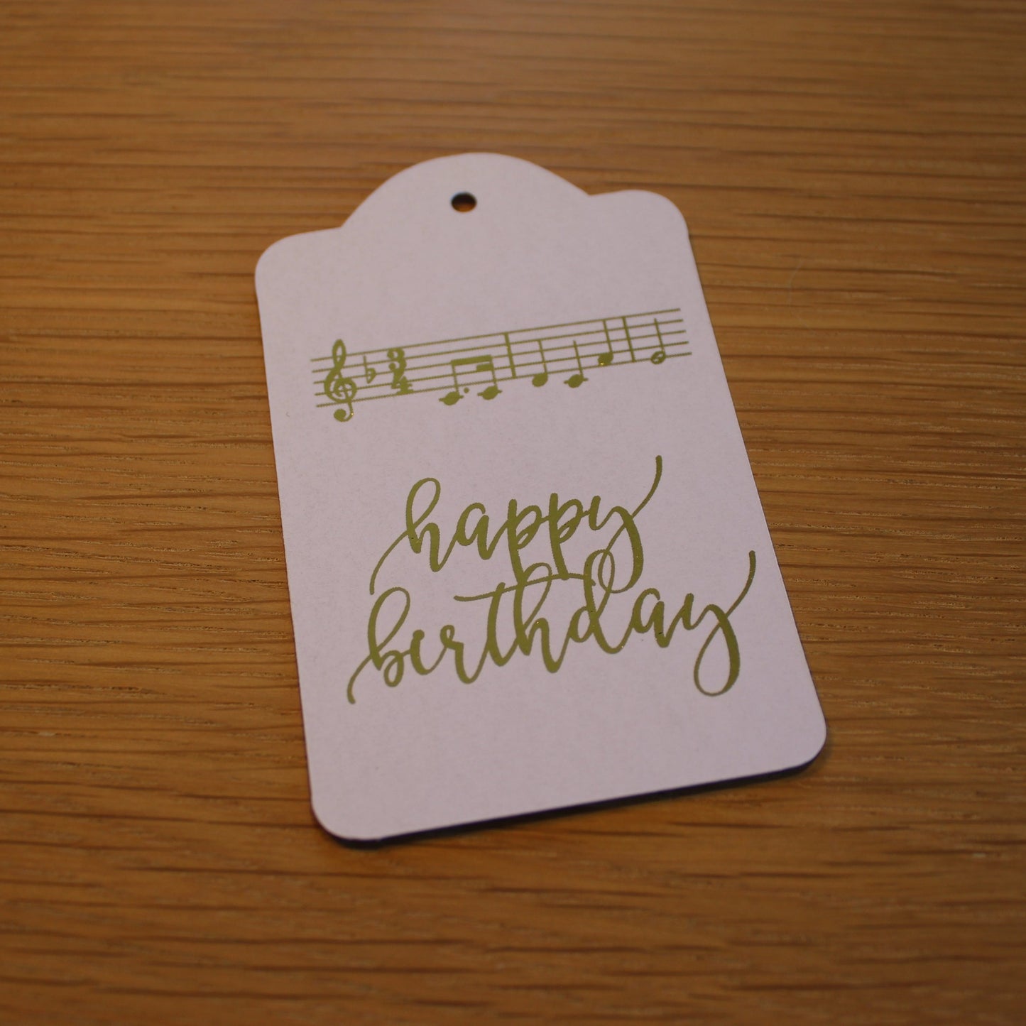 Oblong white tag with 'happy birthday' and the music of 'happy birthday to you' displayed in gold shiny foil.