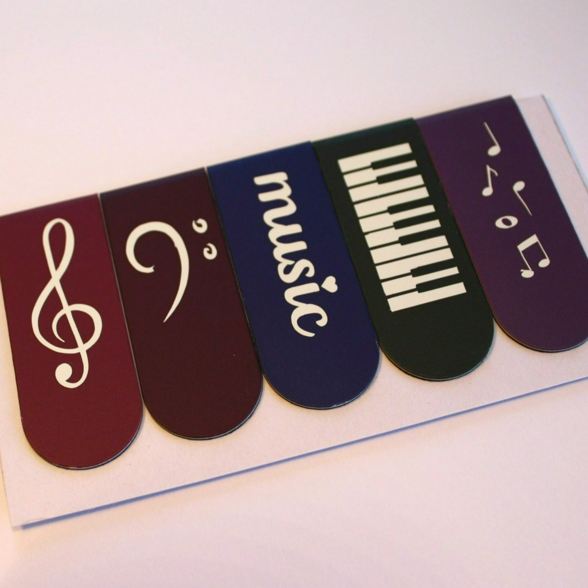 Bookmarks in plum, dark plum, violet, dark grey and purple. Each bookmark has a different symbol; treble clef, piano keys, bass clef, 'music' and music notes.