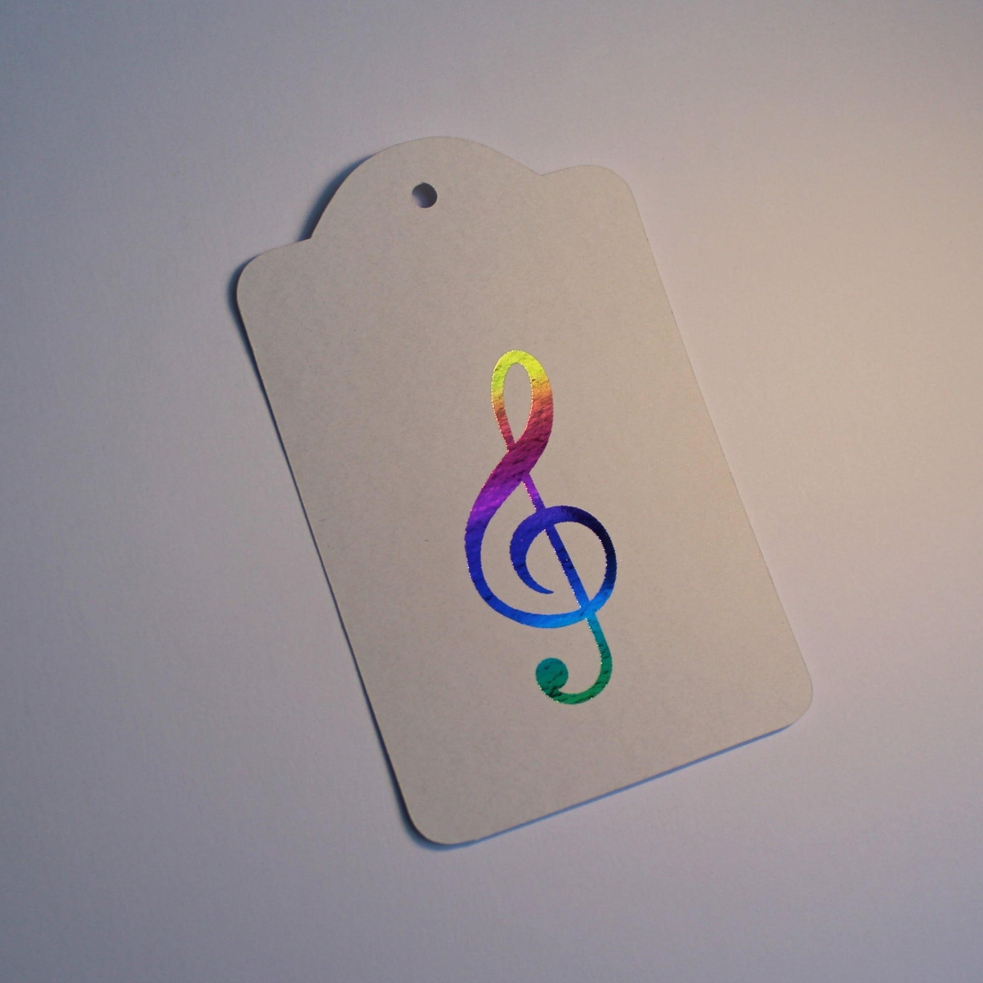 Oblong white tag with a treble clef in the centre, displayed in multicoloured shiny foil.