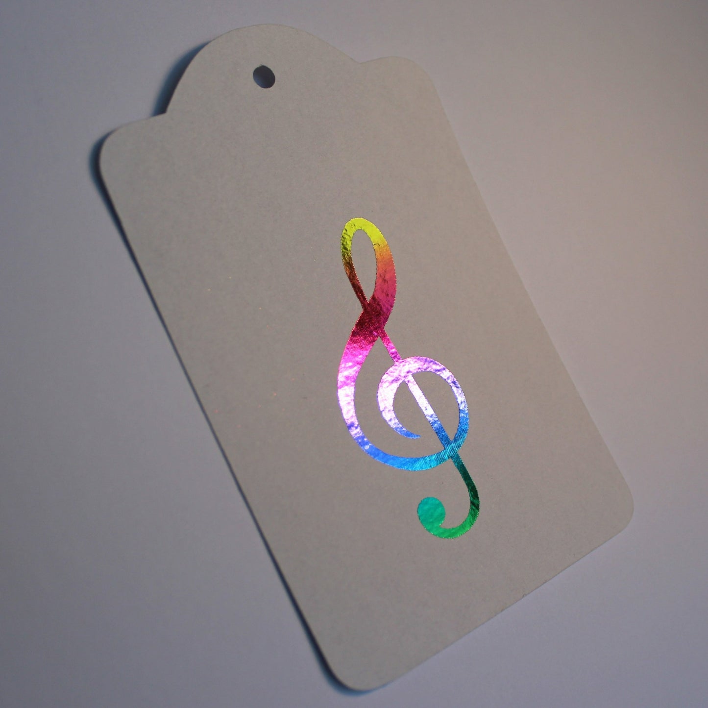 Oblong white tag with a treble clef in the centre, displayed in multicoloured shiny foil.