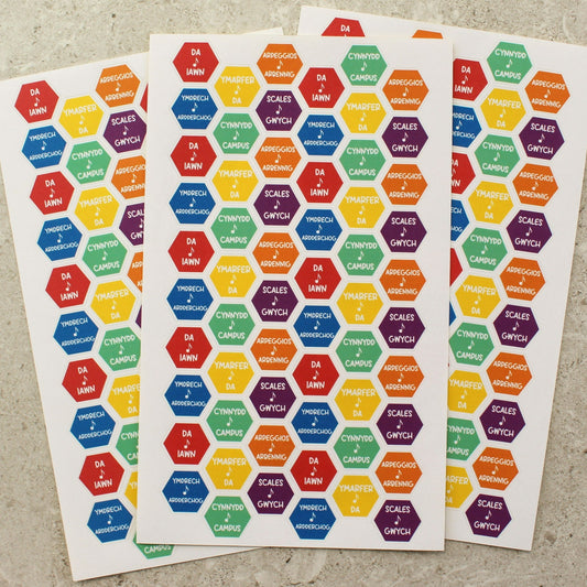 sheets of multicoloured stickers each with a hexagonal design and Welsh wording